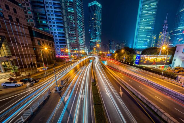 A brightly lit, empty city highway at night. Behind it, the city skyline.