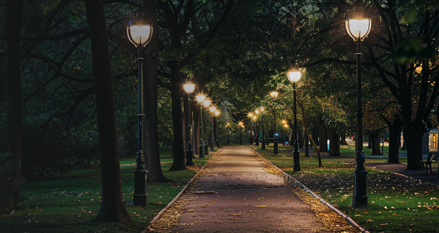 A path through a park at night, the path is illuminated by many street lamps.